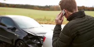 Billede af en skadet bil og en bilist der ringer efter hjælp