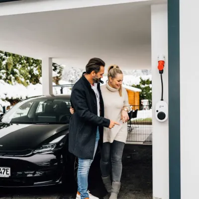 Billede af et par og deres nye elbil hjemme i garagen.